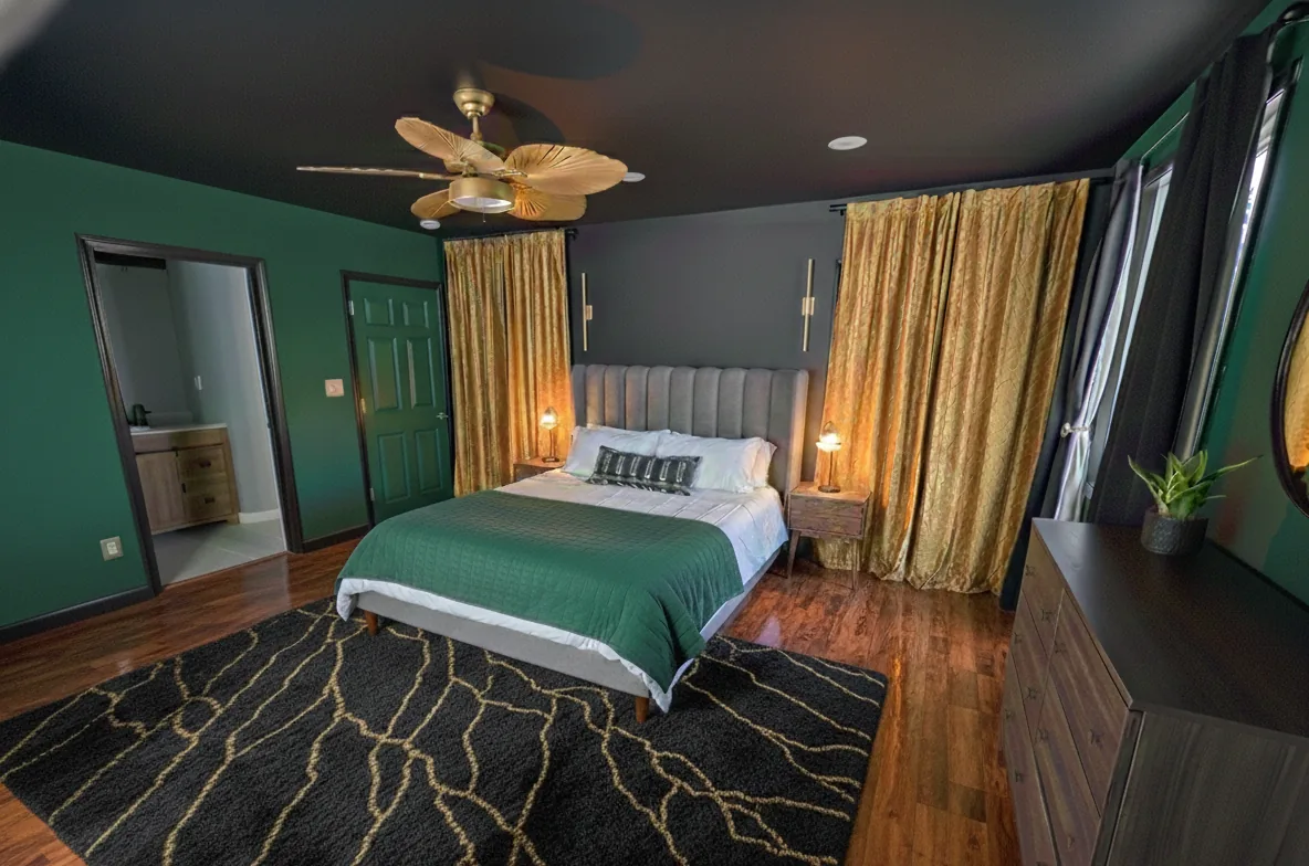 Modern Emerald Master Bedroom Suite - Luxurious master bedroom featuring bold emerald walls, warm gold accents, hardwood flooring, and an ensuite bathroom.